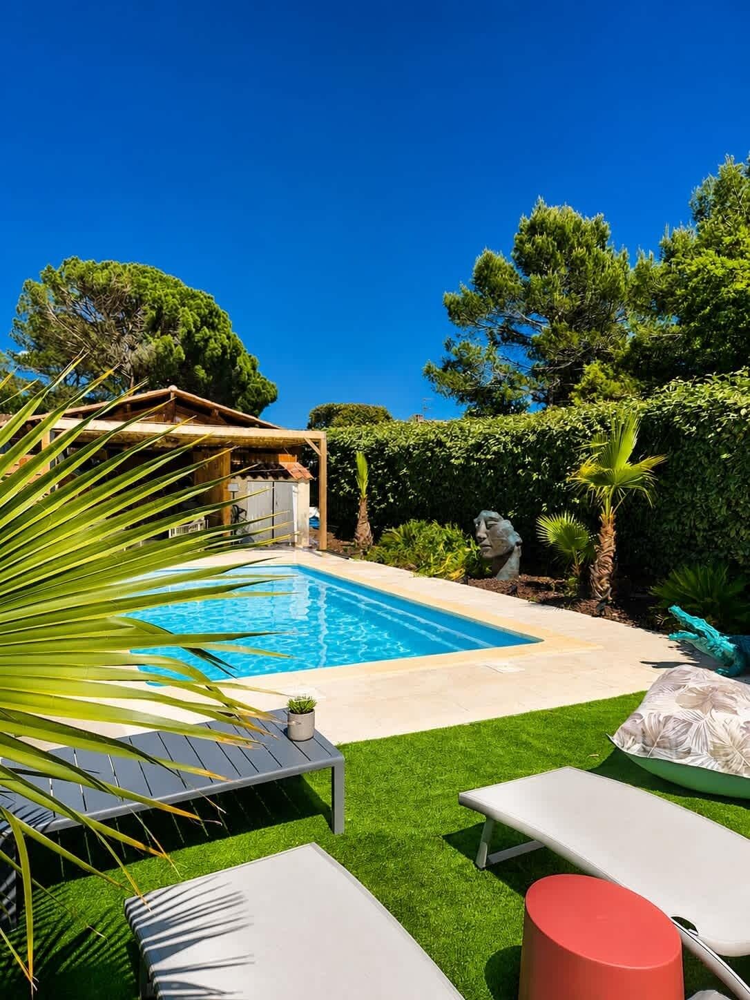 A backyard with a swimming pool, a covered seating area, and a statue.