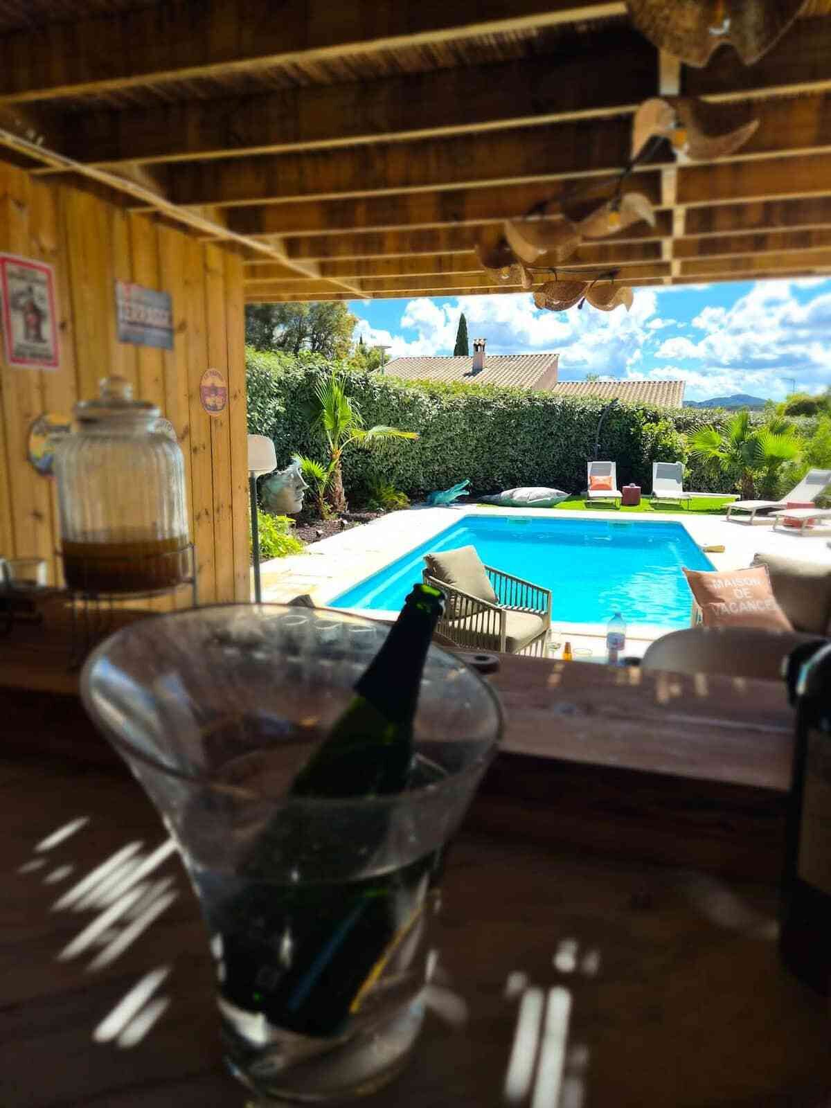 Vista da piscina com uma taça de champanhe, deck de madeira e céu claro.