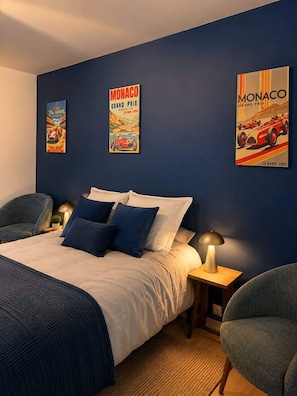 A bedroom with a bed, two chairs, a nightstand, and wall art featuring Monaco Grand Prix posters. - Villa with pool & pool house – AC – 6/8 guests (Roquebrune-sur-Argens)