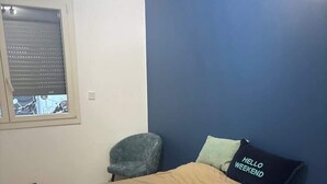 Et soveværelse med seng, stol, vindue og en væg med blå detaljer.