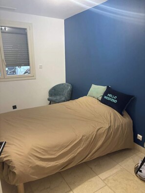 Ein Schlafzimmer mit Bett, Stuhl, Fenster und einer Wand mit blauem Akzent.