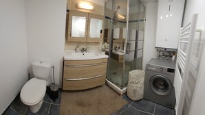 A compact bathroom with a toilet, sink, vanity, glass shower enclosure, and a washing machine. - 🌿Cozy Two-Bedroom Apartment in Aix-en-Provence (2 people)🌿 (Aix-en-Provence)
