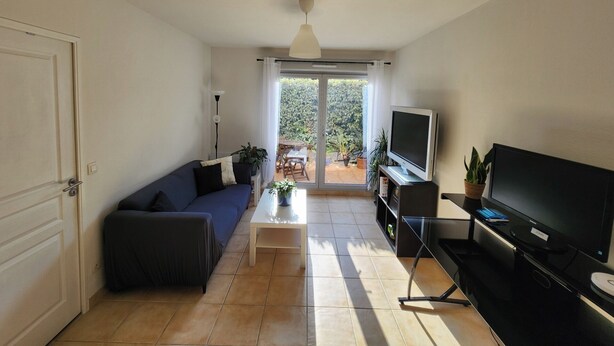A living room with a sofa, television, and a sliding glass door leading to an outdoor area. - 🌿Cozy Two-Bedroom Apartment in Aix-en-Provence (2 people)🌿 (Aix-en-Provence)