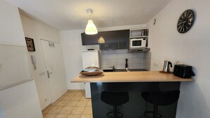 A compact kitchen with a central island, bar stools, a microwave, and a clock on the wall. - 🌿Cozy Two-Bedroom Apartment in Aix-en-Provence (2 people)🌿 (Aix-en-Provence)