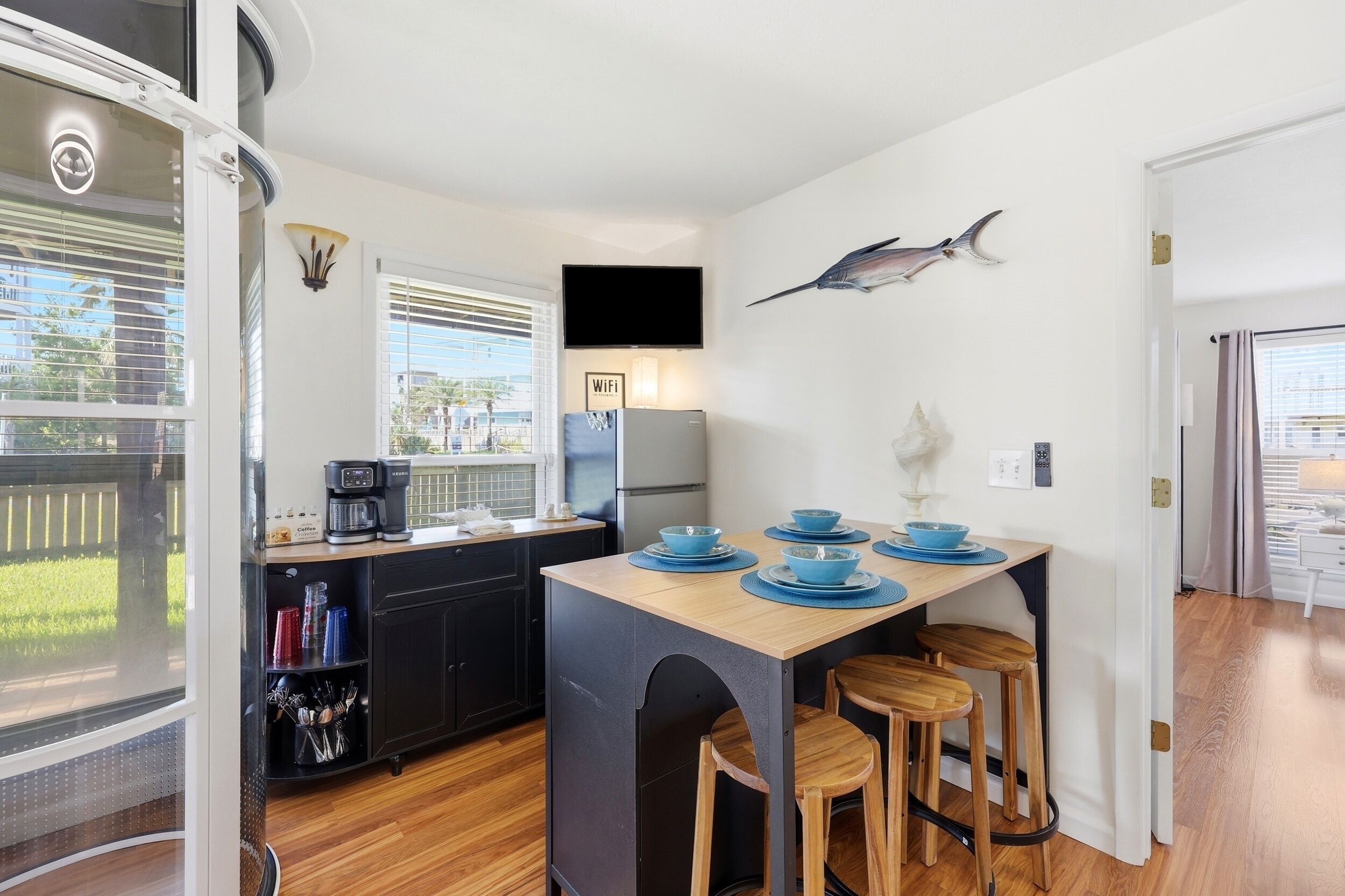 A compact kitchen with a central island, bar stools, a flat-screen TV, and a mounted fish decoration.