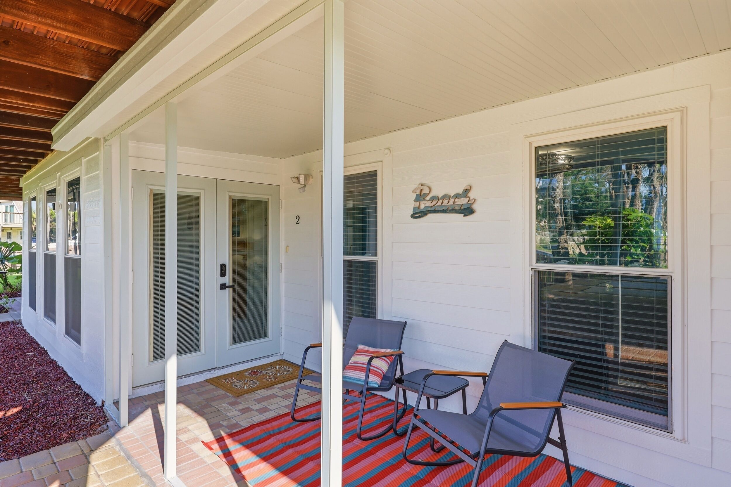 A covered porch with two chairs, a red and blue striped rug, and a 'Pool' sign on the wall.