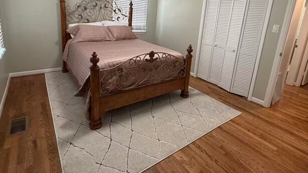 Quarto com cama de madeira, armário branco e janela com persianas.