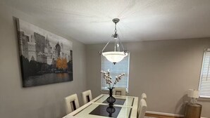 Uma sala de jantar com mesa, cadeiras, um lustre e uma pintura da cidade na parede.