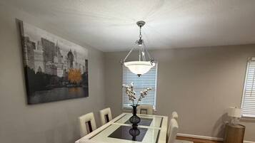 A dining area with a table, chairs, a chandelier, and a cityscape painting on the wall.