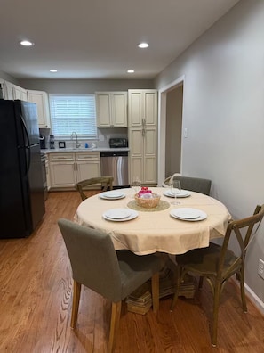 A dining area with a round table set for four, surrounded by wooden chairs.