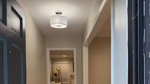 Um corredor com piso de madeira, um tapete, uma porta e um lustre.