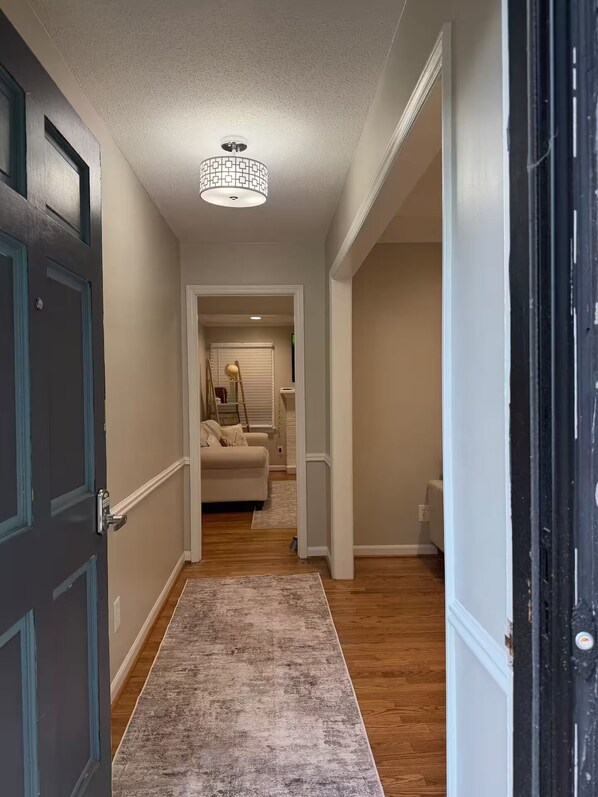 A hallway with a wooden floor, a rug, a door, and a ceiling light fixture.