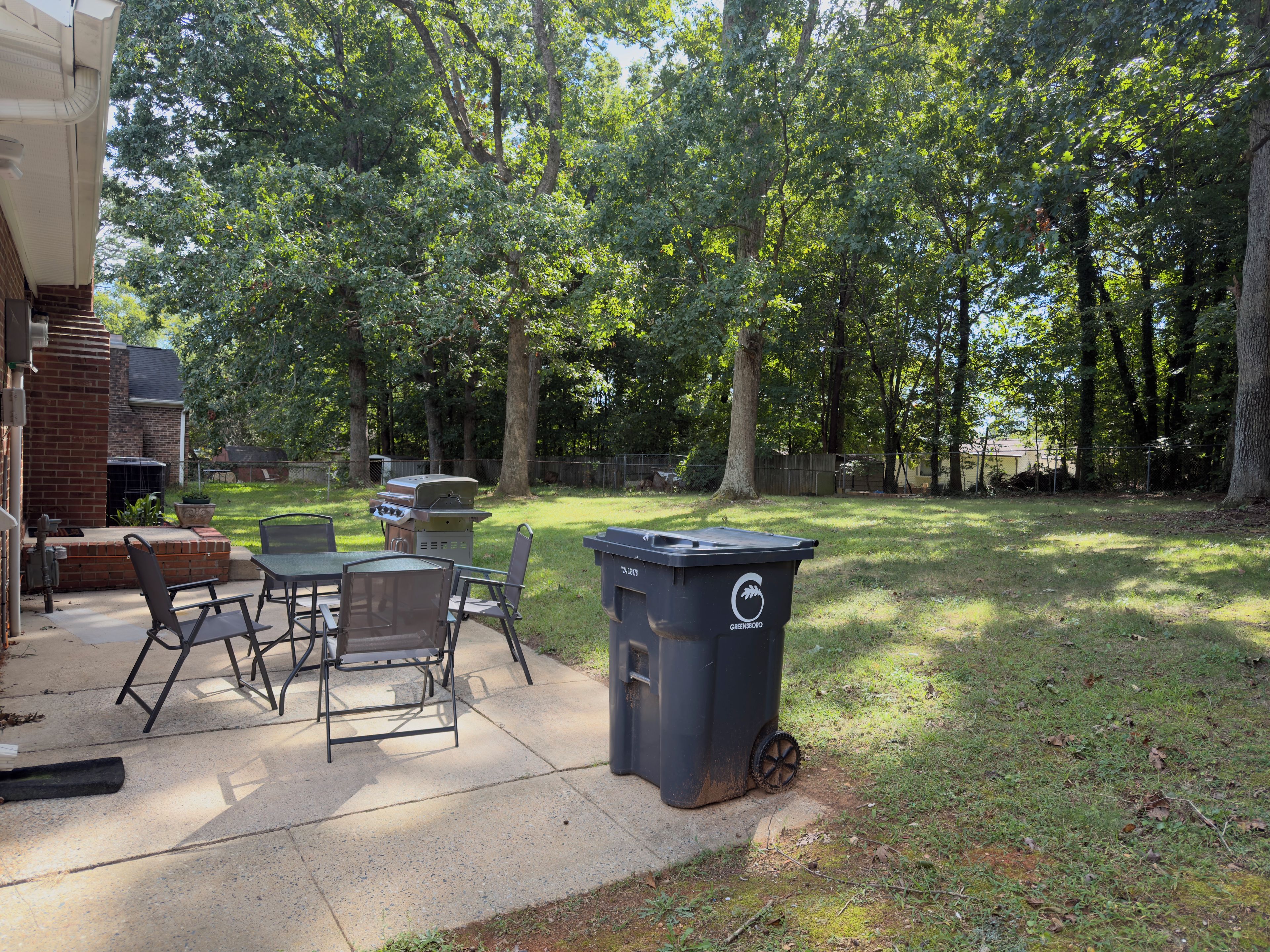 A backyard with a barbecue grill, outdoor seating, and a trash bin.