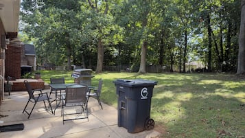 A backyard with a barbecue grill, outdoor seating, and a trash bin.