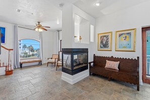 Ein geräumiges Wohnzimmer mit Kamin, einer Bank, einem Sofa und Blick ins Freie.