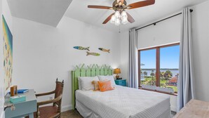 Ein Schlafzimmer mit einem Bett, einem Sessel, einem Schreibtisch, einem Deckenventilator und einem Fenster mit Blick.