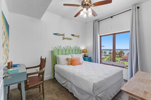 Ein Schlafzimmer mit einem Bett, einem Sessel, einem Schreibtisch, einem Deckenventilator und einem Fenster mit Blick.