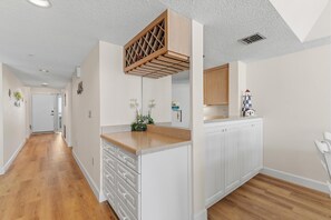 Une cuisine moderne avec des meubles blancs, un îlot central en bois et un plafond orné d’un motif géométrique original.