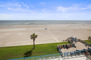 A beach with a clear sky, a palm tree, and a boardwalk with chairs and umbrellas. - Ebb Tide 406 (New Smyrna Beach)