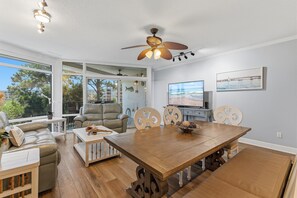 A spacious living room with a large wooden dining table, comfortable seating, a ceiling fan, and a television. - Marker 33 #1c3 (New Smyrna Beach)