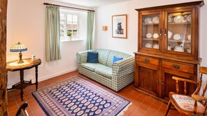 A cozy room with a checkered sofa, a wooden cabinet with glass doors, a patterned rug, and a table with a lamp. - Coastal Family House for 8 in Cornwall (Axminster)