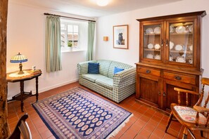 A cozy room with a checkered sofa, a wooden cabinet with glass doors, a patterned rug, and a table with a lamp. - Coastal Family House for 8 in Cornwall (Axminster)