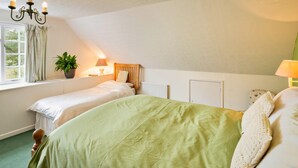 A bedroom with two single beds, a large bed, a window with curtains, a plant on the windowsill, and a radiator. - Coastal Family House for 8 in Cornwall (Axminster)