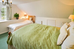 A bedroom with two single beds, a large bed, a window with curtains, a plant on the windowsill, and a radiator. - Coastal Family House for 8 in Cornwall (Axminster)