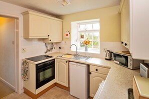 A compact kitchen with white cabinetry, a built-in oven, a dishwasher, and a microwave. - Coastal Family House for 8 in Cornwall (Axminster)