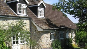 A stone house with a tiled roof, a garden with a bench and table, and a small wheelbarrow. - Coastal Family House for 8 in Cornwall (Axminster)