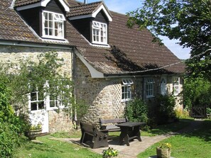A stone house with a tiled roof, a garden with a bench and table, and a small wheelbarrow. - Coastal Family House for 8 in Cornwall (Axminster)