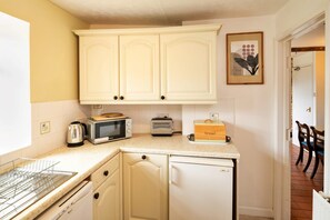 A compact kitchen with white cabinetry, a microwave, a toaster, a bread box, and a small refrigerator. - Coastal Family House for 8 in Cornwall (Axminster)
