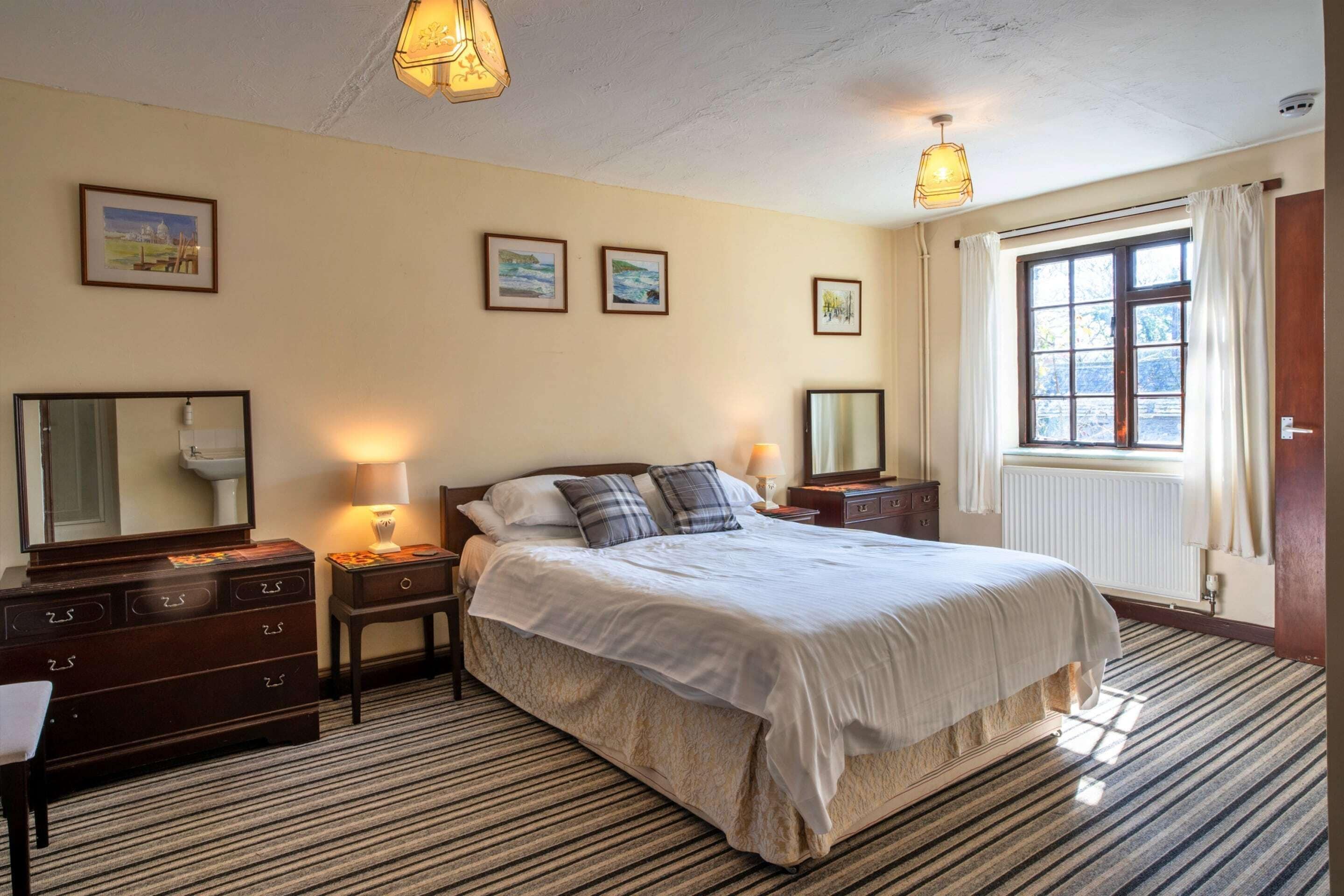 A hotel room with a large bed, two bedside tables, a dresser, a mirror, and a window with curtains.