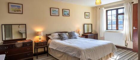 A hotel room with a large bed, two bedside tables, a dresser, a mirror, and a window with curtains.