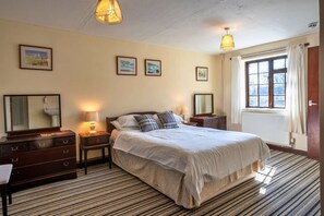 A hotel room with a large bed, two bedside tables, a dresser, a mirror, and a window with curtains. - Modern Plymouth Apartment Near The Hoe (Ilfracombe)