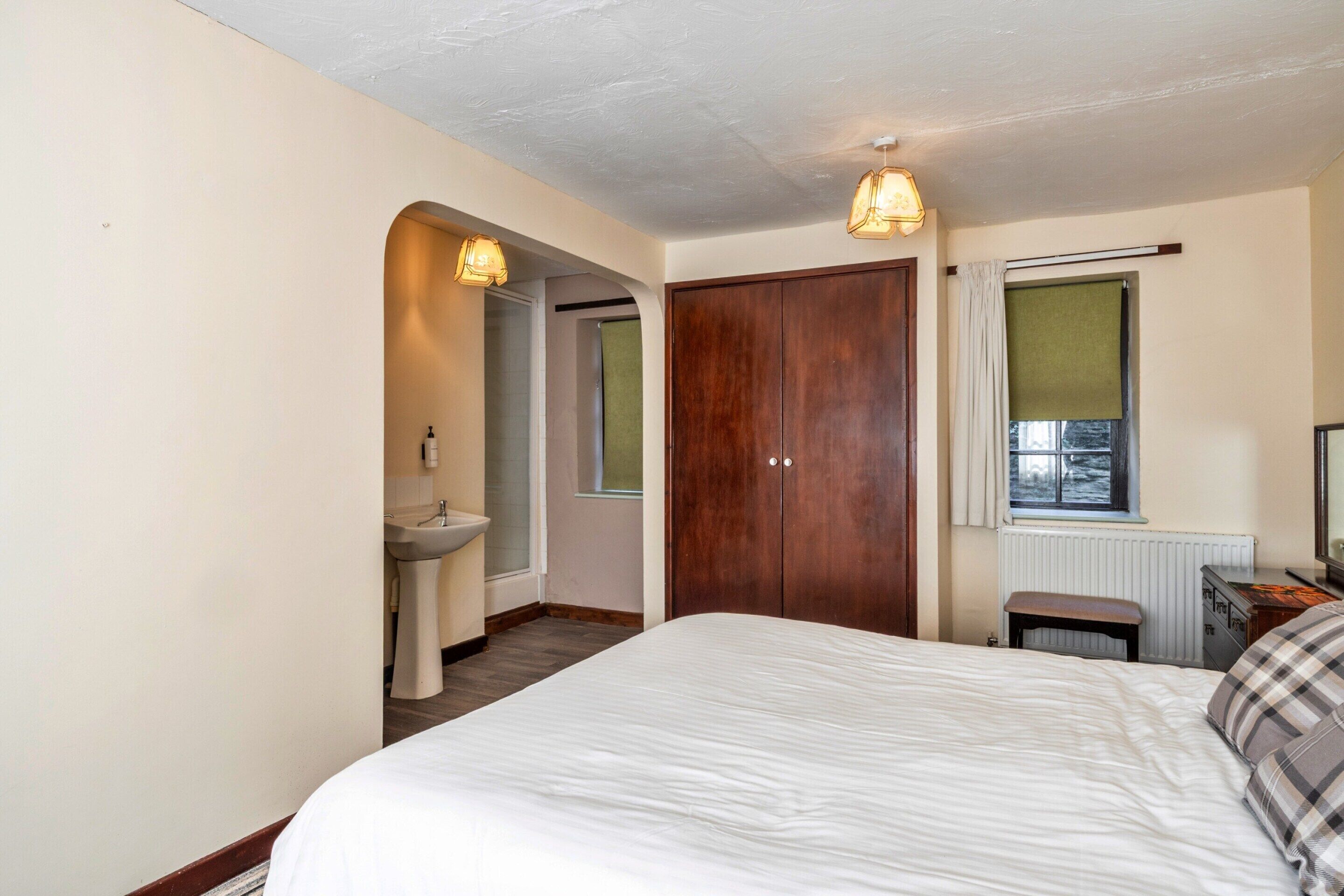 A bedroom with a bed, a wooden wardrobe, a window with a view, and a bathroom with a sink and shower.