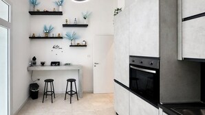 A modern kitchen with a built-in oven, a coffee bar, and two stools. - Natia Sicily Villa Anita (Sicilia)