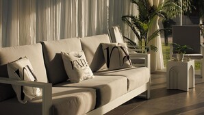 A modern living room with a sofa, pillows, a side table, and a potted plant. - Natia Sicily Villa Anita (Sicilia)