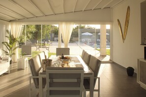 A dining area with a table set for four, chairs, and a view of the outdoors through large glass doors. - Natia Sicily Villa Anita (Sicilia)