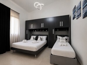 A modern bedroom with two beds, a large wardrobe, and a unique ceiling light fixture. - Natia Sicily Villa Anita (Sicilia)