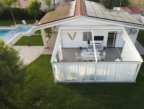 Ein modernes Haus mit überdachter Terrasse, Pool und gepflegtem Rasen.