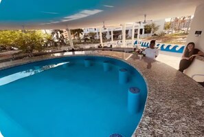 A swimming pool with a tiled edge, a lounge area with seating, and a view of the surrounding buildings. - Pets love sandy beach at casa blanca (Puerto Peñasco)