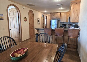 A dining area with a wooden table and chairs, a bowl of fruit, and wooden cabinets in the background. - Pets love sandy beach at casa blanca (Puerto Peñasco)