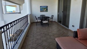 A balcony with a dining table and chairs, a sofa, and a painting on the wall. - Pets love sandy beach at casa blanca (Puerto Peñasco)