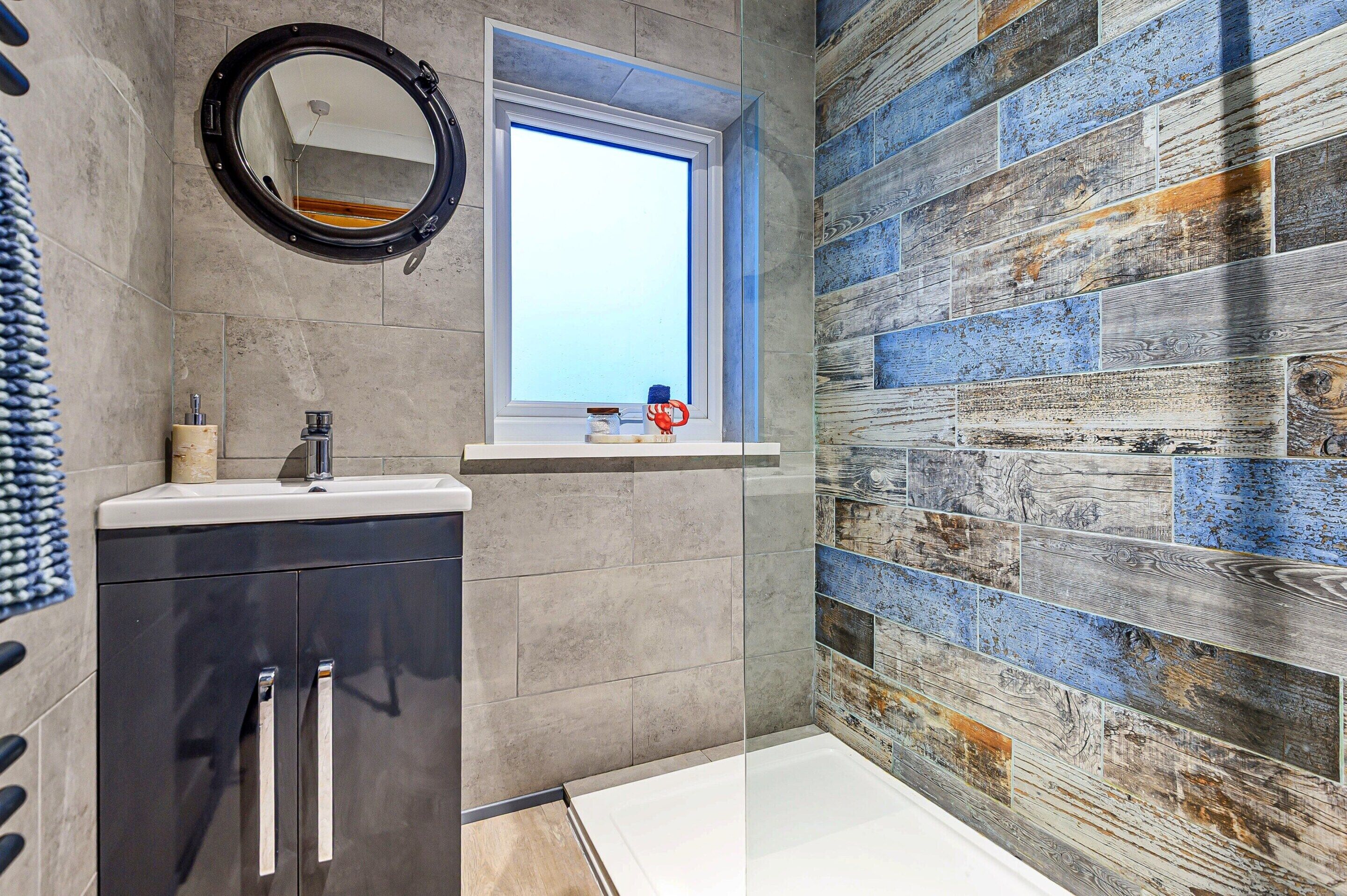 A bathroom with a modern design, featuring a round mirror, a window, and a wooden-textured wall.