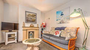 A living room with a sofa, a television, a fireplace, and artwork on the walls. - Welcoming Cottage Near Harbour (Whitby)