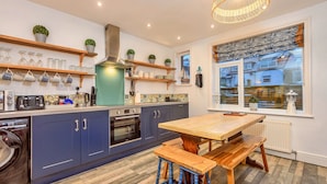 A modern kitchen with blue cabinets, a wooden table, and a window with a view of a snowy landscape. - Welcoming Cottage Near Harbour (Whitby)