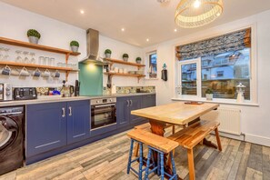 A modern kitchen with blue cabinets, a wooden table, and a window with a view of a snowy landscape. - Welcoming Cottage Near Harbour (Whitby)