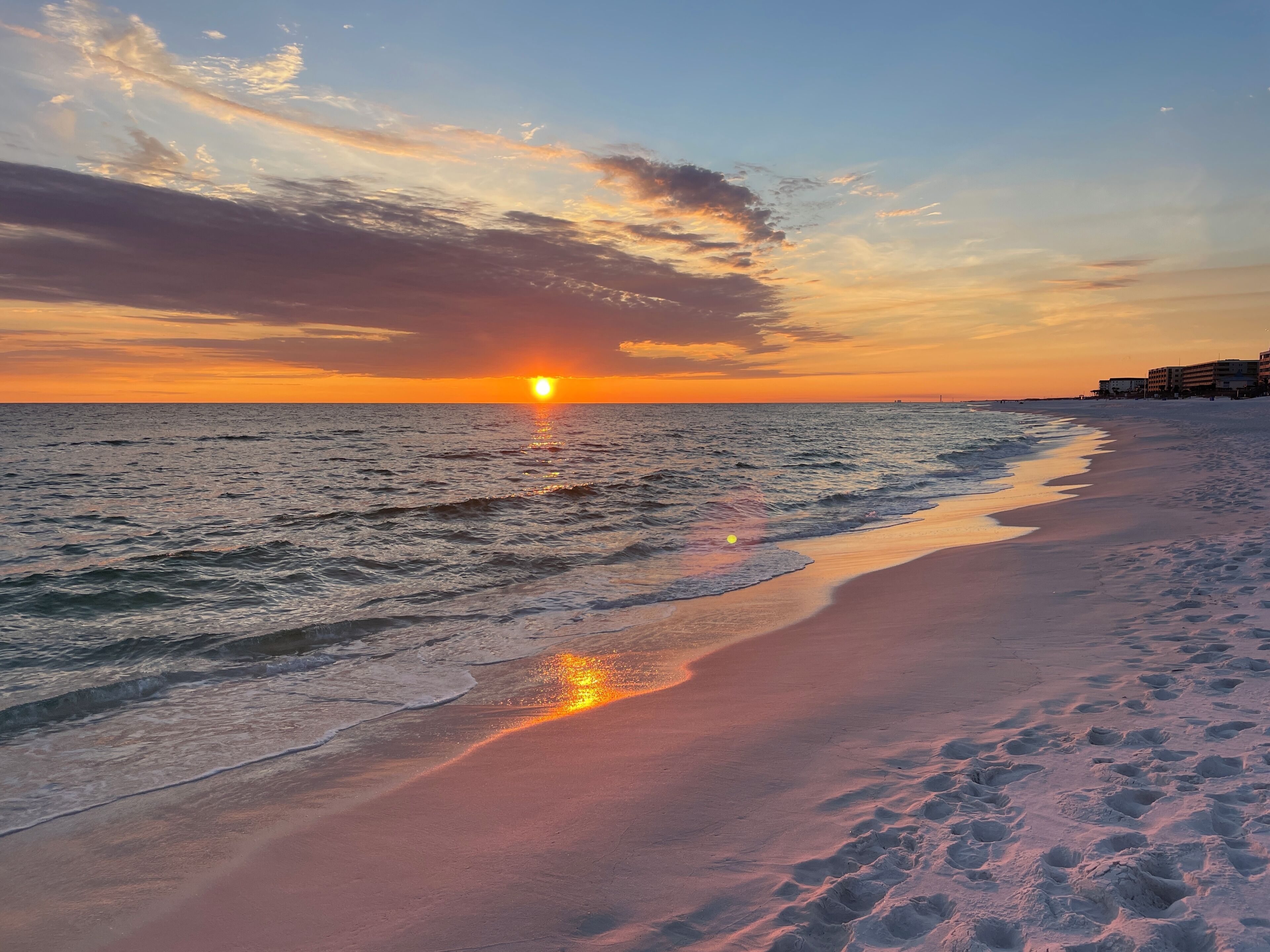 Ein Strand bei Sonnenuntergang, Wellen und Fußabdrücke im Sand.