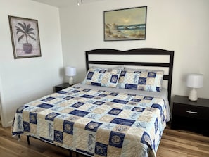 A bedroom with a bed, two bedside tables, a nightstand, a wall-mounted painting, and a potted plant. - 3-Min Walk to Beach! King + 2 Queens, 2.5 Baths  • Sleeps 6 (Fort Walton Beach)